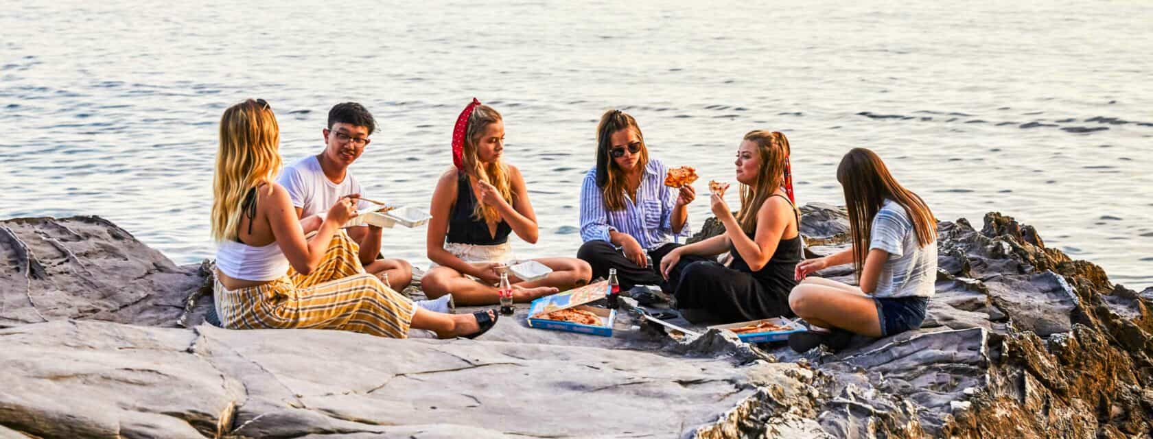 Students eating food by the ocean.