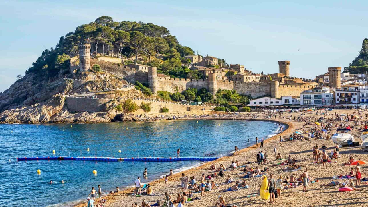 A beach with a castle on a hill in the background.